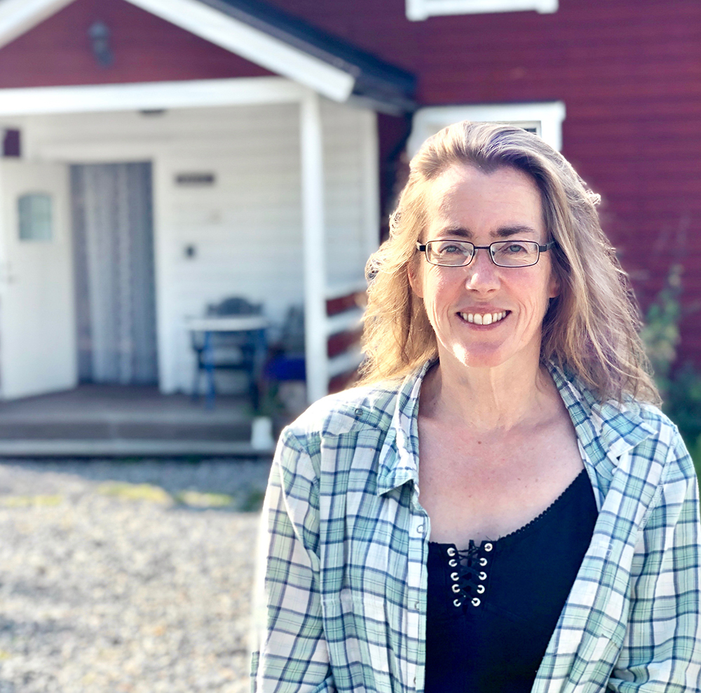 En leende kvinna, i bakgrunden delar av ett rött hus